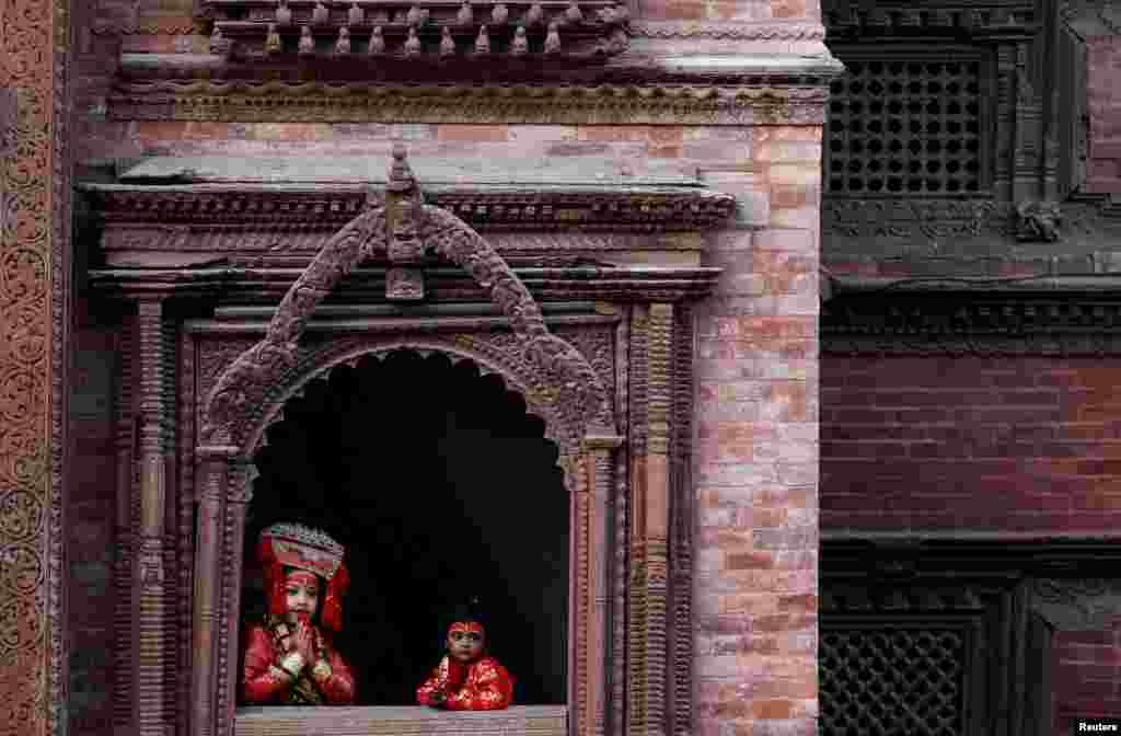 Young girls dressed as the Living Goddess Kumari look through the window of a temple during the Kumari Puja, in Kathmandu, Nepal.