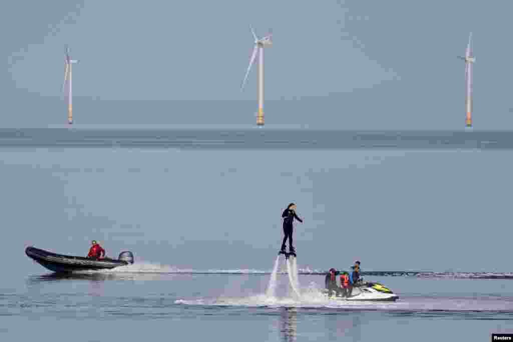A speedboat passes a person using a flyboard near a wind farm on an unseasonably hot day in Herne Bay, Britain, Oct. 8, 2023.