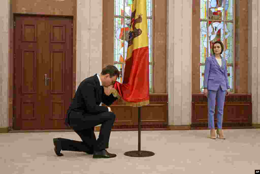 Moldova's president Maia Sandu, right, watches as Prime Minister Dorin Recean kneels down in front of the national flag during a swearing-in ceremony in Chisinau.