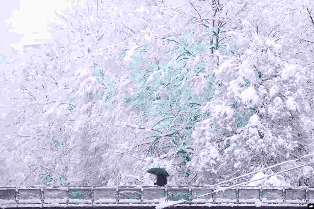 A man carrying an umbrella, crosses a bridge during heavy snowfall in Sarajevo, Bosnia.