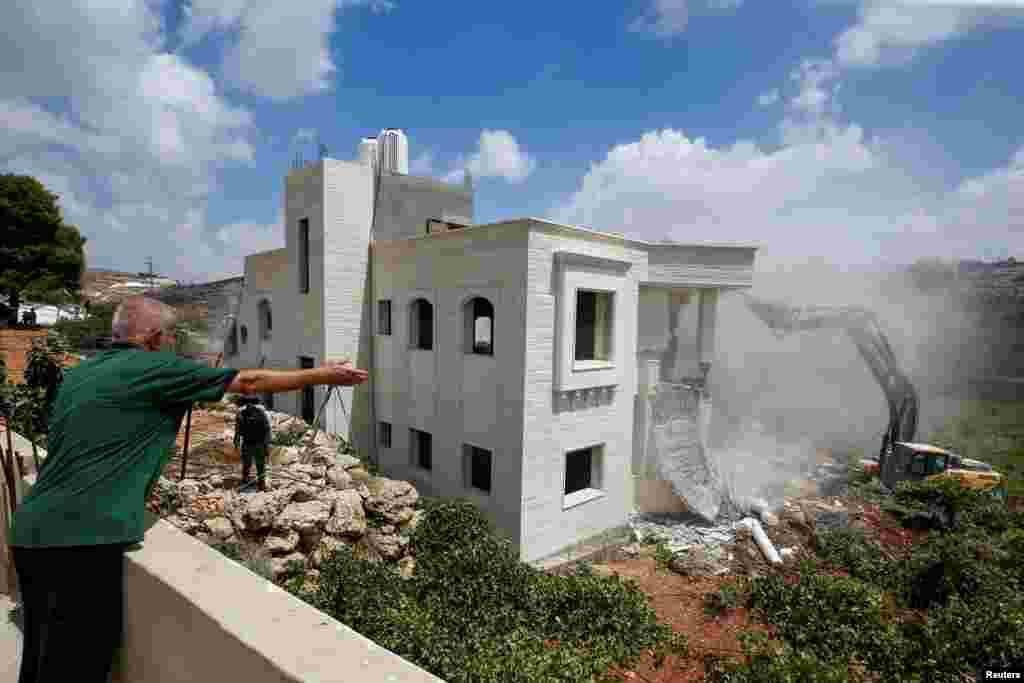 A Palestinian man gestures as an Israeli machinery guarded by Israeli forces demolishes a Palestinian house in Hebron in the Israeli-occupied West Bank.
