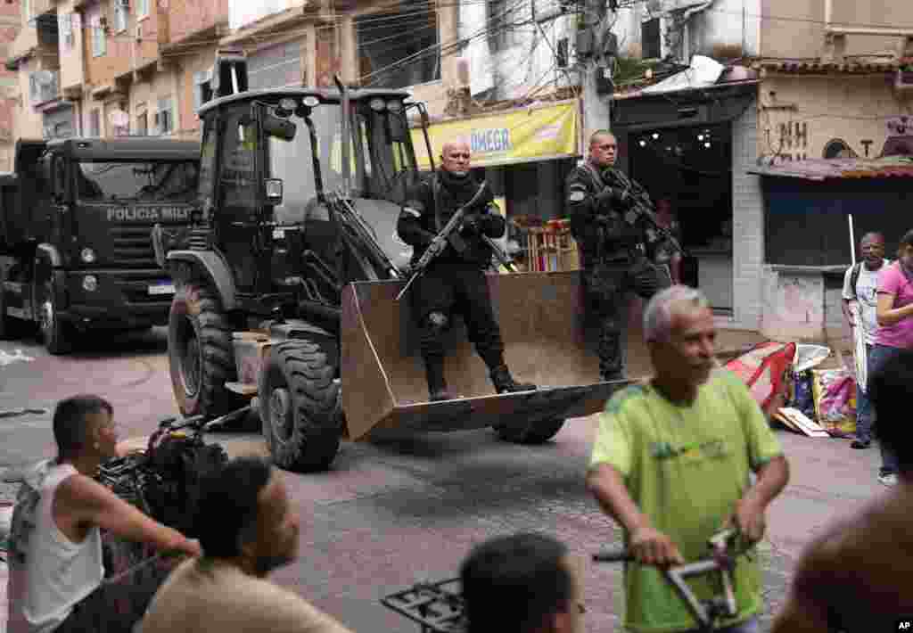 Police ride past residents in a bulldozer they use to clear street barricades during a security operation against organized crime in the Mare Complex favela of Rio de Janeiro, Brazil.