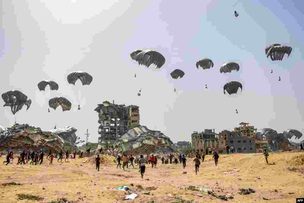 People rush toward humanitarian aid packages dropped near destroyed buildings in the northern Gaza Strip, amid the ongoing conflict in the Palestinian territory between Israel and the militant group Hamas.