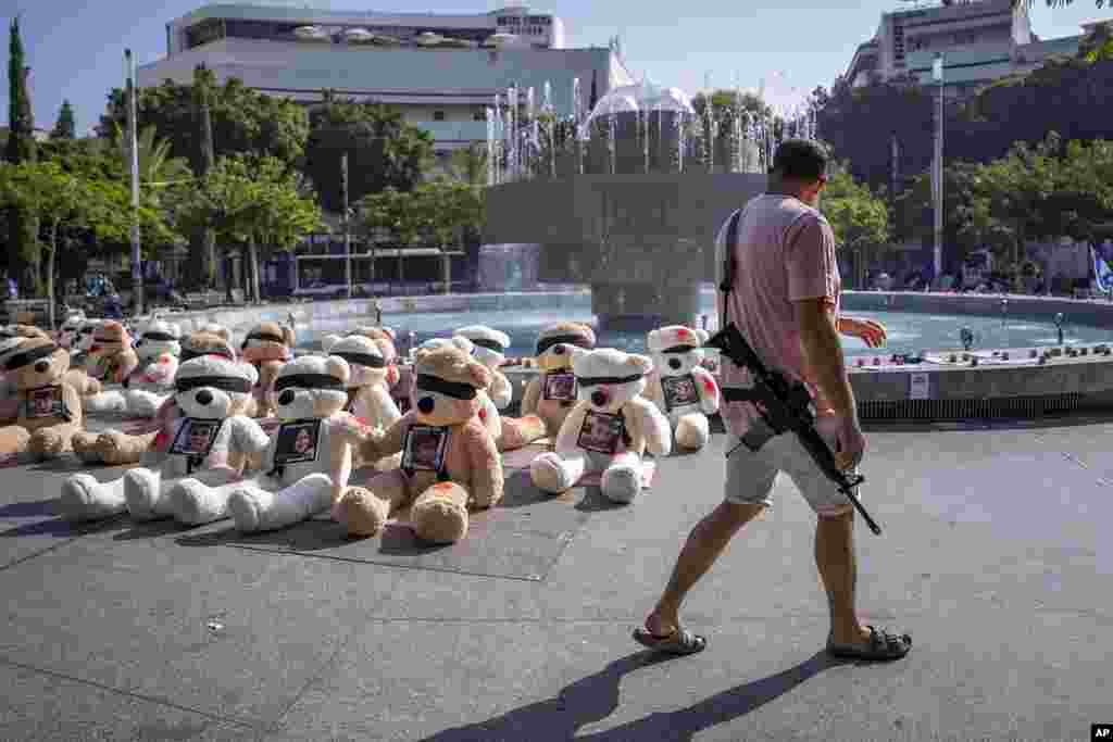 An off-duty Israeli soldier walks by an installation of blindfolded giant teddy bears adorned with photos of Israelis held captive in Gaza, in Tel Aviv, Israel. The installation is meant to draw attention to over 200 people who were abducted by Hamas militants during a bloody and unprecedented October 7 cross-border attack.