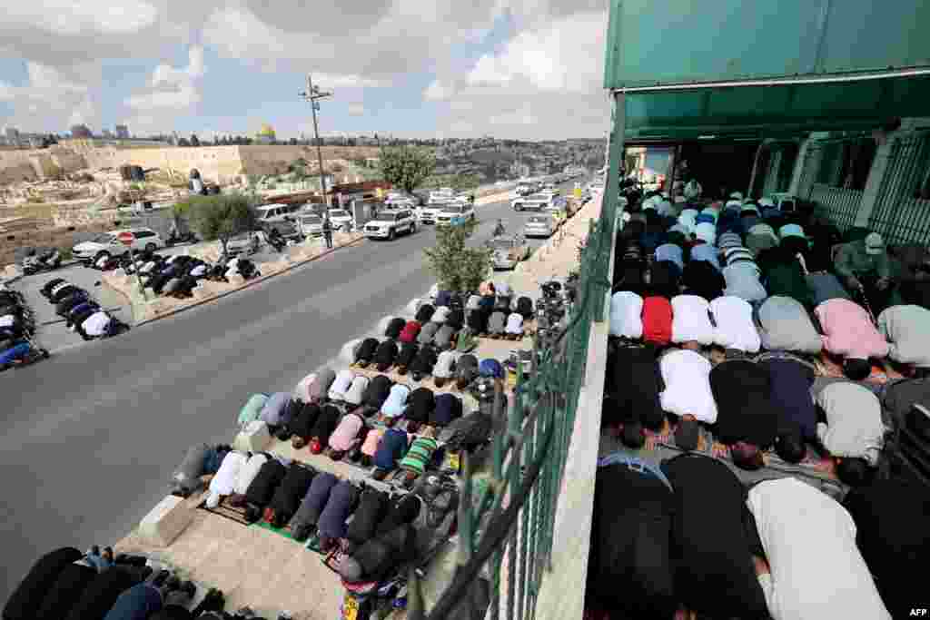 Muslim Palestinians take part in Friday Noon prayers in East Jerusalem neighborhood of Ras al-Amud, following age restrictions by Israeli security to above 50 years old for worshippers wanting to access the Al-Aqsa Mosque compound, top background, amid the ongoing battles between Israel and the Palestinian group Hamas. 