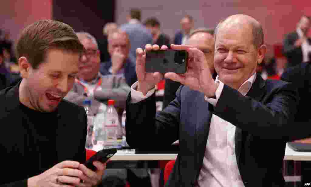 German Chancellor Olaf Scholz, right, and Secretary General of Germany's Social Democratic SPD party Kevin Kuehnert share a smile as they use their mobile phones during the party congress of Germany's social democratic SPD party in Berlin.