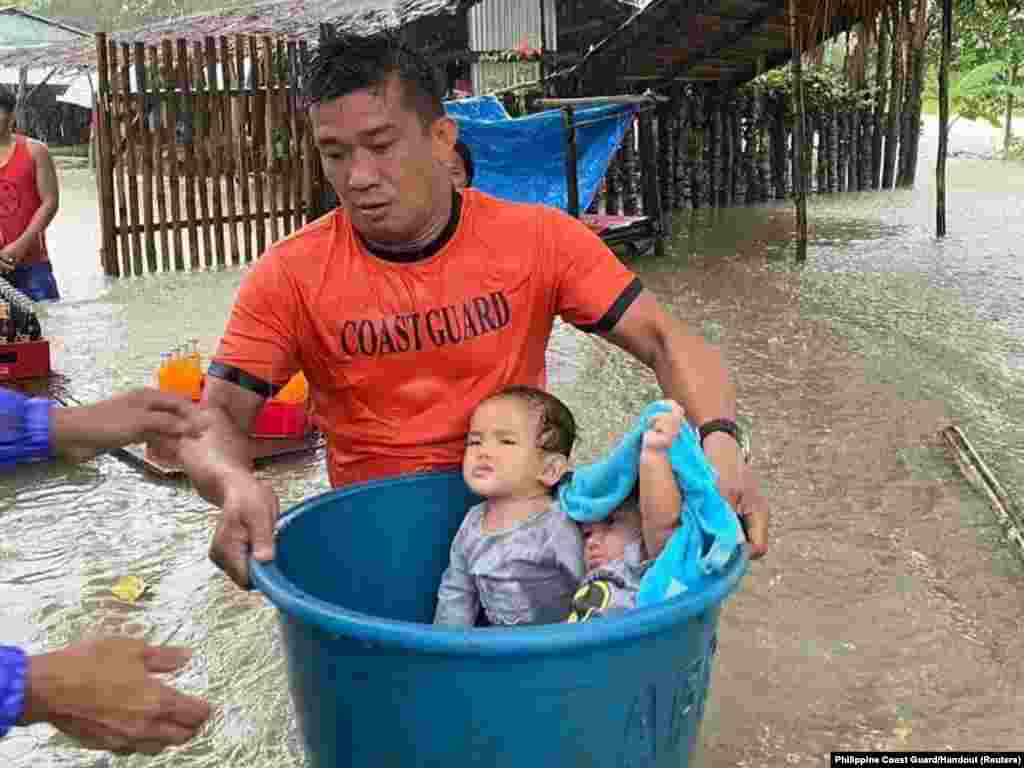 A member of the Philippine Coast Guard carries children affected by floods on a basin during a rescue operation, in Zamboanga City, Zamboanga province.