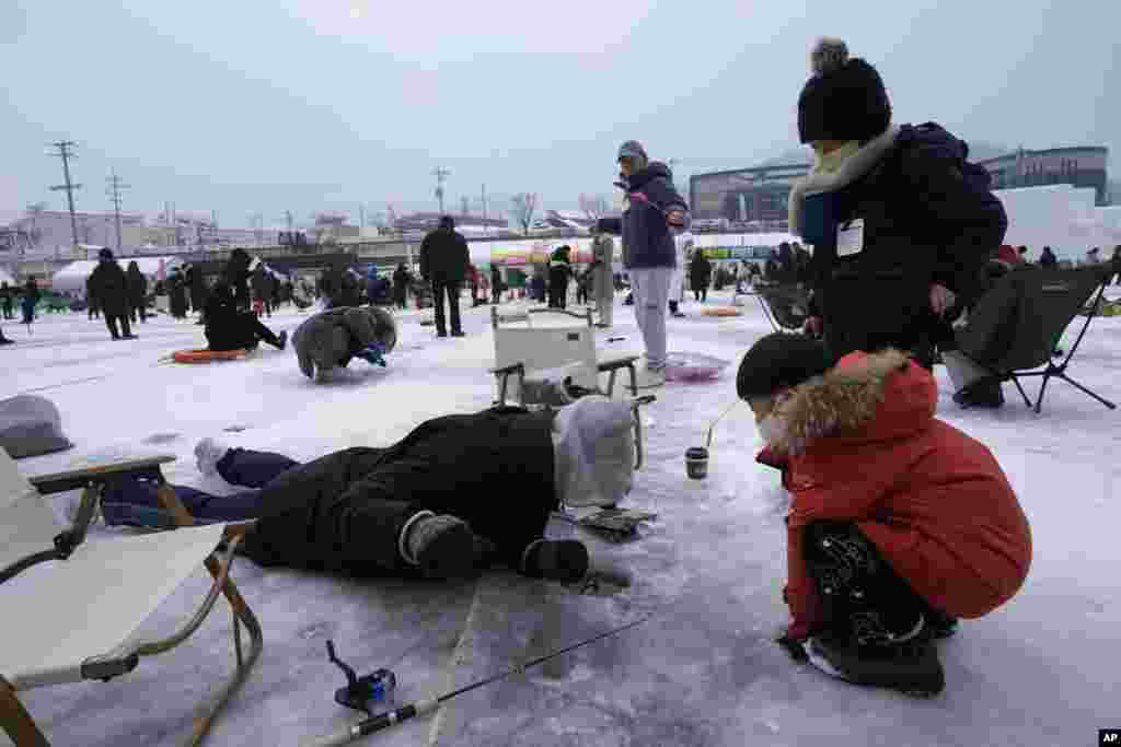 A man casts a line through a hole drilled in the surface of a frozen river during a trout catching contest in Hwacheon, South Korea, Jan. 7, 2023.
