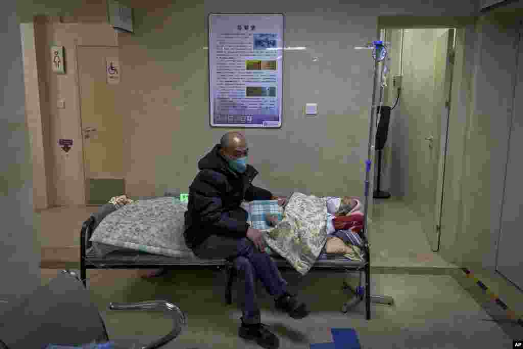 A man wearing a face mask tends to his elderly relative in a corridor of the emergency ward at a hospital in Beijing, China. As COVID-19 continues to rip through China, global organizations and governments have called on the country start sharing data.