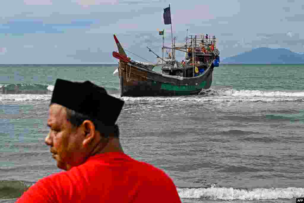 A man stands near a boat used by Rohingya refugees to arrive in Lamnga beach, Aceh province, Indonesia. A wooden boat carrying nearly 200 Rohingya refugees, a majority of them women and children, landed on Indonesia's western coast, police said.