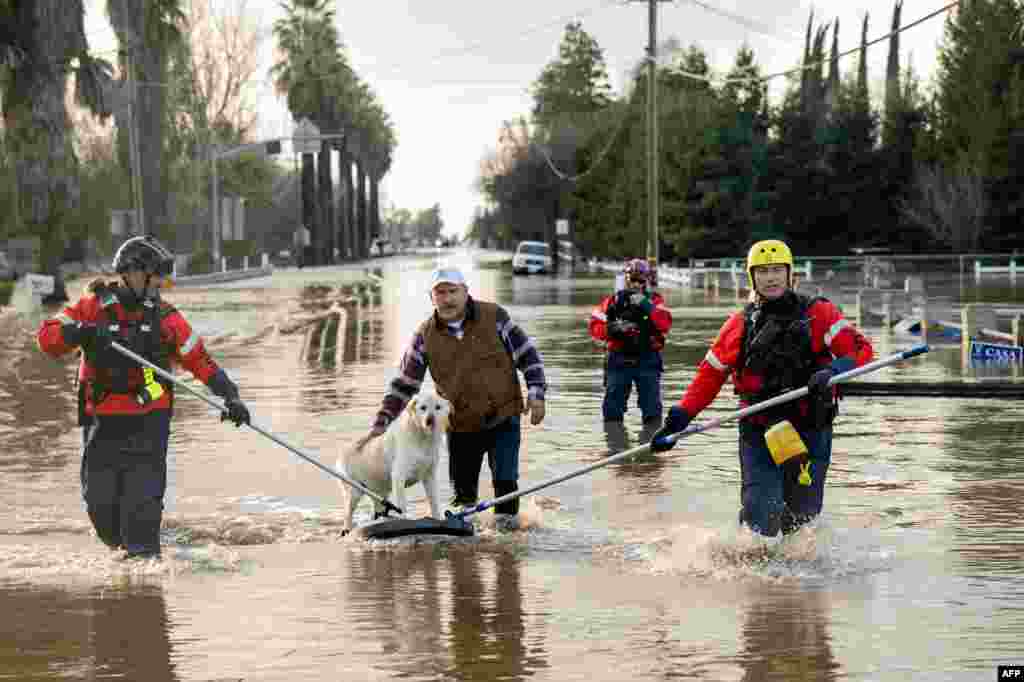 San Diego firefighters help Humberto Maciel rescue his dog from his flooded home in Merced, California, Jan. 10, 2023. Relentless storms were ravaging California again, the latest bout of extreme weather that has left 14 people dead. Fierce storms caused flash flooding, closed key highways, toppled trees and swept away drivers and passengers. 