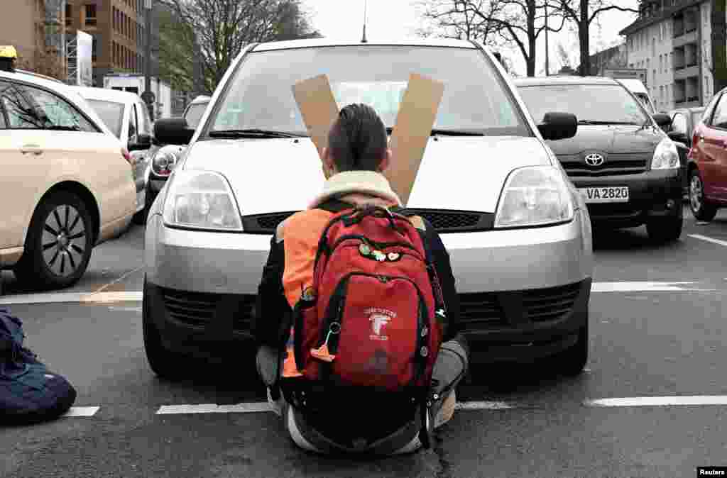 A car stands directly in front of a climate change activist who is glued to a street and blocks the traffic during rush hour in Cologne, Germany.