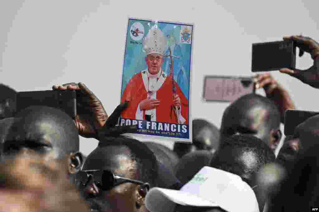 A man holds a picture of Pope Francis as a crowd gathers to welcome him upon his arrival at the Juba International Airport in Juba, South Sudan.