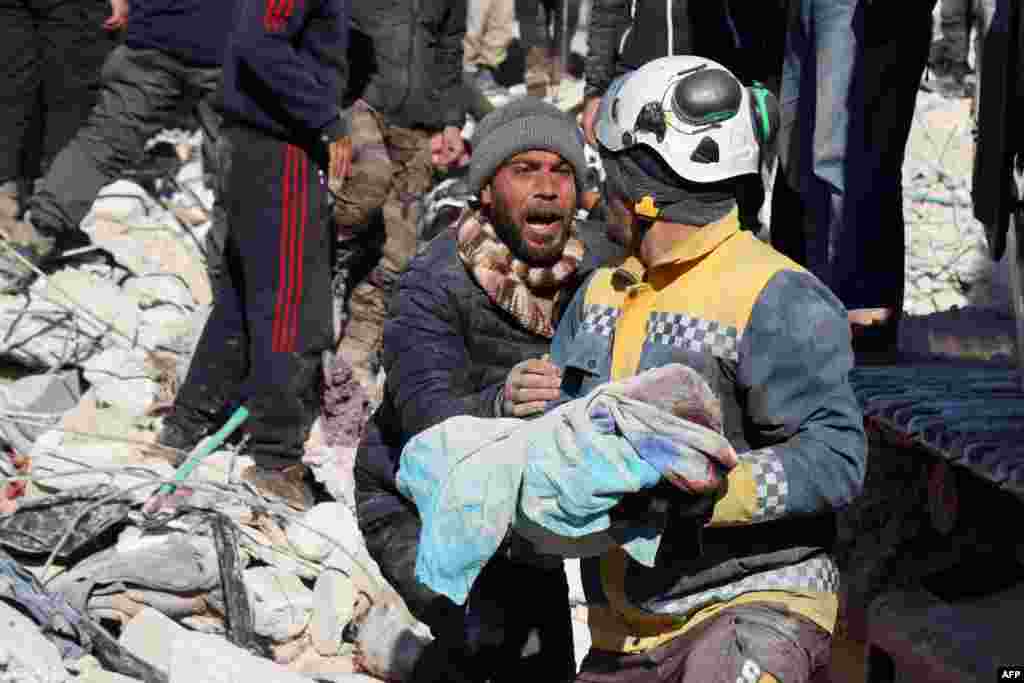 A man reacts as the body of his baby pulled out from the rubble, is taken away by a White Helmet rescue worker, in the town of Harim in Syria's rebel-held northwestern Idlib province.