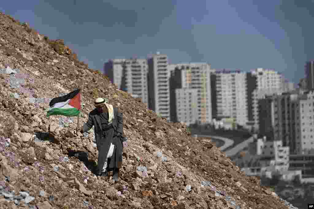 An elderly Palestinian walks with a Palestinian flag during a demonstration against a new Israeli settlement in the village of Qalandia near the West Bank city of Ramallah.