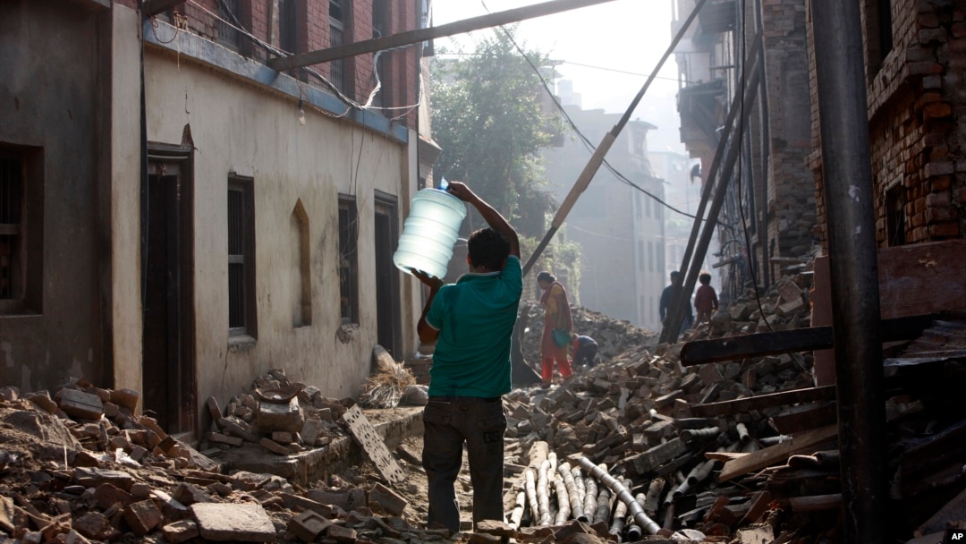 A Nepalese man carrying a water jar walks past damaged houses in Bhaktapur, Nepal, May 14, 2015. 