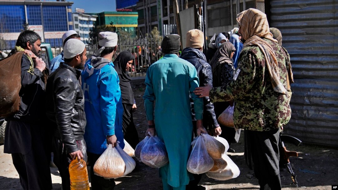 FILE - Afghans carry food supplies during a distribution of humanitarian aid for families in need, in Kabul, Afghanistan, Feb. 16, 2022.