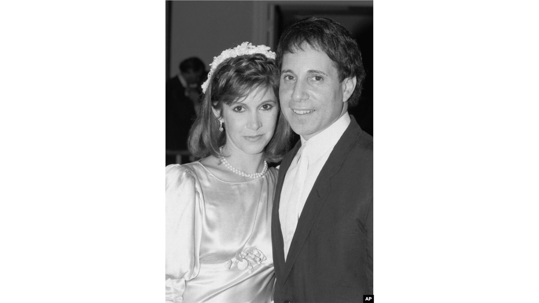 FILE - Actress Carrie Fisher and singer Paul Simon pose in a doorway of the midtown New York City apartment where their wedding reception was in progress, Aug. 16, 1983.