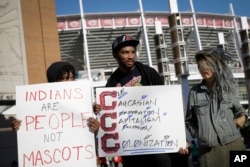 FILE - Protesters against the Cleveland Indians team name picket outside Great American Ball Park before a baseball game between the Cincinnati Reds and the Indians, May 19, 2016, in Cincinnati.