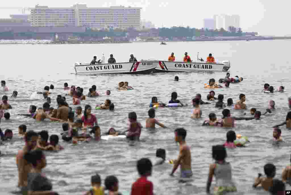 Penjaga pantai Filipina berjaga-jaga di luar Kedutaan Besar AS dekat orang-orang yang berenang pada hari libur Paskah di Manila. (AP/Aaron Favila)