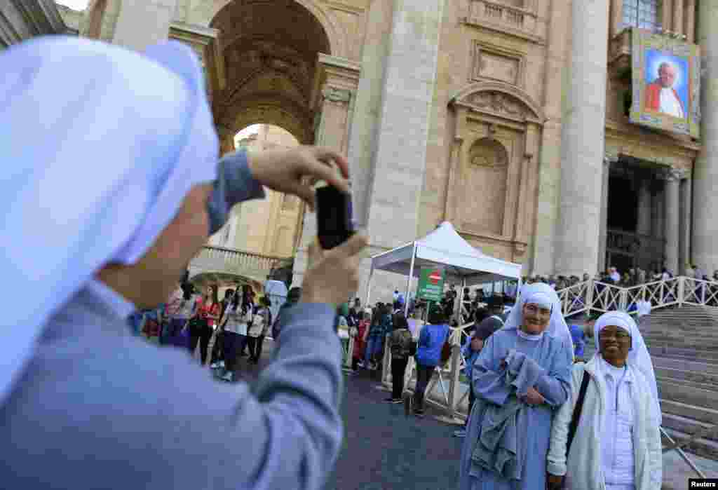 Dua biarawati berpose di depan tapestry yang menampilkan gambar Paus Yohanes Paulus II di St. Peter's Square di Vatikan. 