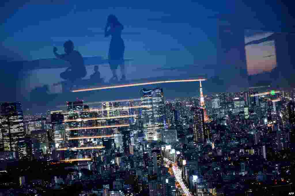 The Tokyo Tower (centre R) is illuminated as visitors are reflected in glass while visiting the Shibuya Sky observation deck in Tokyo, Japan.