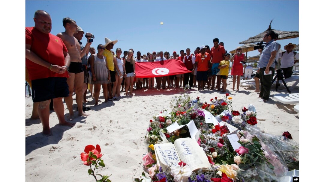 People, some displaying a Tunisian flag, stand in silence next to flowers during a gathering at the scene of the attack in Sousse, Tunisia, June 28, 2015.