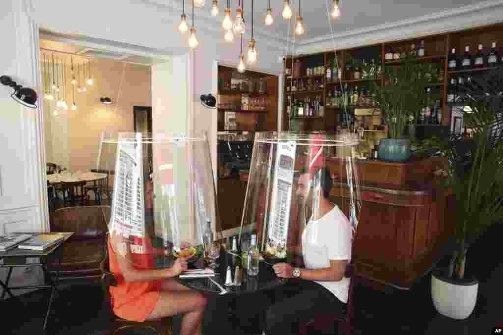 A man and a woman demonstrate dining under a plastic shield in a restaurant of Paris. As restaurants in food-loving France prepare to reopen, some are investing in lampshade-like plastic shields to protect diners from the coronavirus.