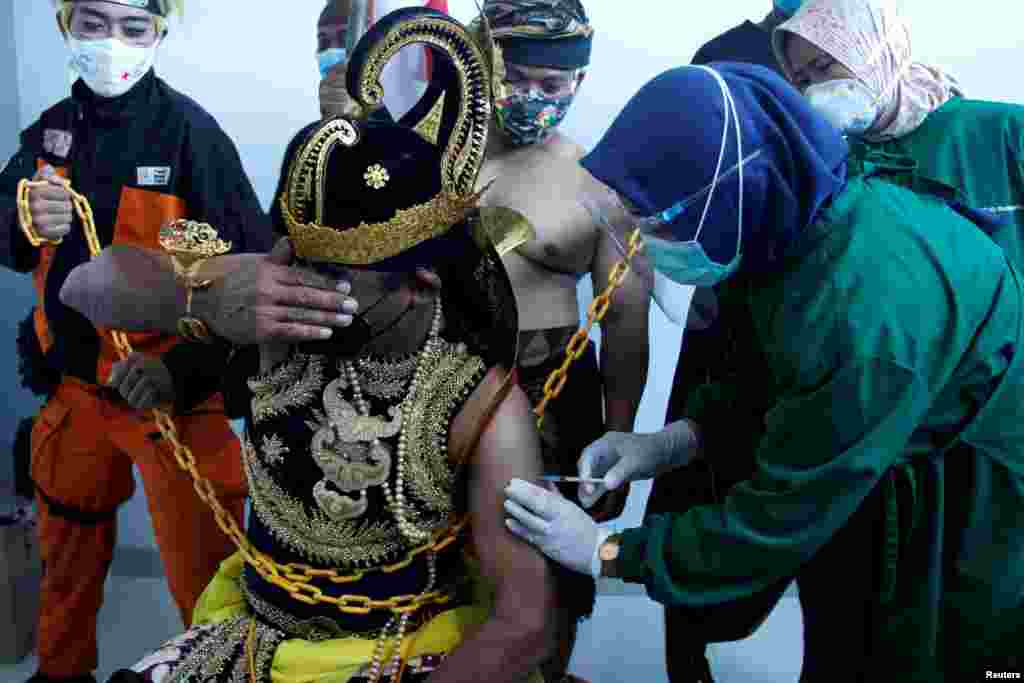 An Indonesian health care worker injects Sinovac's vaccine to a man dressed in Indonesia's traditional human puppet costume known as Wayang, as Indonesia drives mass vaccination for COVID-19, in Central Java province, Indonesia. (Antara Foto/via Reuters)