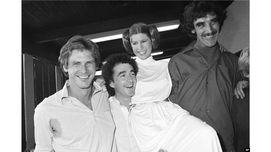 FILE - Actor Harrison Ford, left, who played Han Solo in the move "Star Wars," is pictured with his co-stars, Anthony Daniels, who played C-3P0; Carrie Fisher, who played Princess Leia; and Peter Mayhew, who played Chewbacca, as they take a break from filming a television special, Oct. 5, 1978.