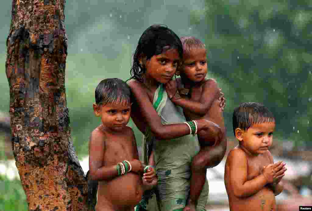 Children take shelter under a tree as it rains in New Delhi, India.