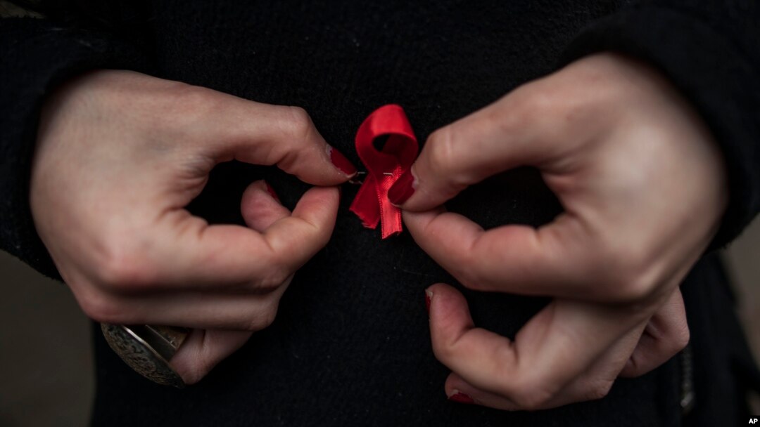 A woman adjusts a red ribbon, symbol of the fight against AIDS during a demonstration on World Aids Day, in Pamplona northern Spain, Dec. 1, 2014.