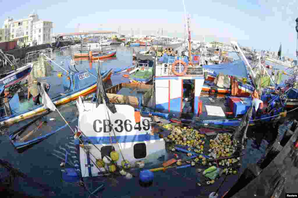 Para nelayan memeriksa kapal-kapal yang tenggelam setelah gempa dan tsunami yang melanda pelabuhan Iquique di Chile utara (2/4).