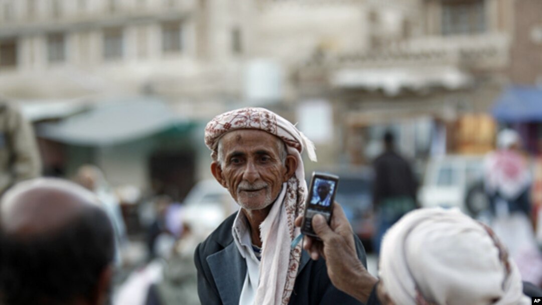 A Yemeni man, right, uses his mobile phone to take photos of his friend as they gather near the historical site of Bab al-Yemen in the the old city of Sana'a, Yemen, Nov. 14, 2012.