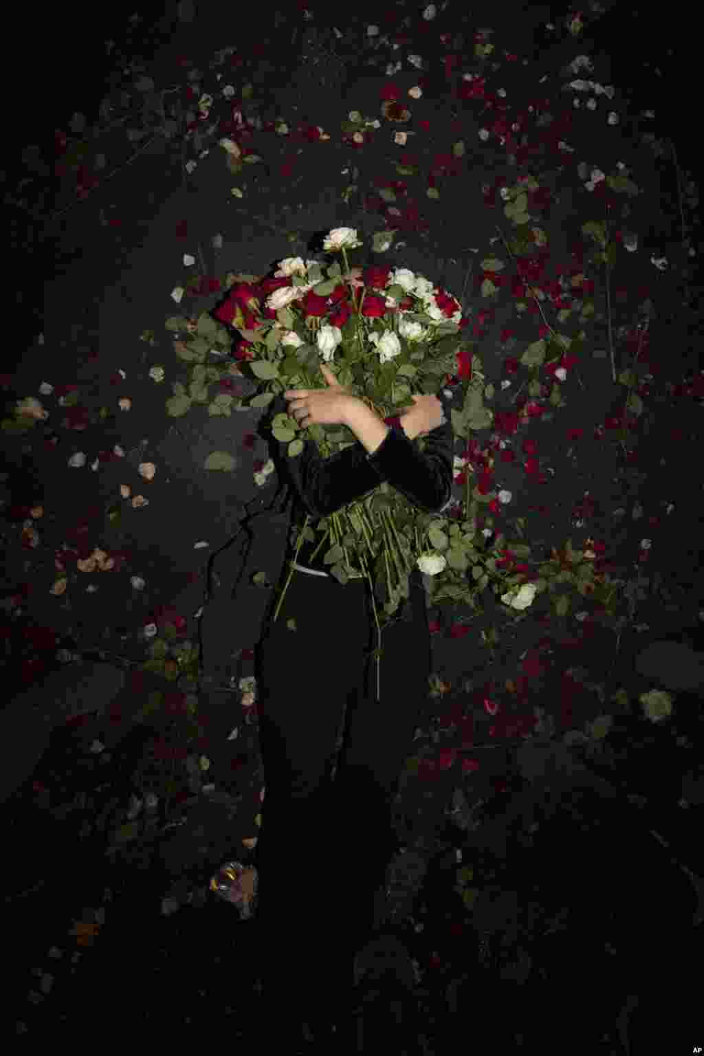 An Israeli protester holds flowers as she lies on the road during a demonstration against Prime Minister Benjamin Netanyahu near the Prime Minister's residence in Jerusalem, Aug. 15, 2020.