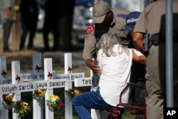 Los policías ayudan a una mujer después de presentar sus respetos frente a las cruces con los nombres de los niños asesinados esta semana en la Escuela Primaria Robb en Uvalde, Texas, el jueves 26 de mayo de 2022.