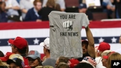 FILE - A Trump supporter holds a T-shirt reading "You Are Fake News" before a rally by President Donald Trump in Rochester, Minn., Oct. 4, 2018. 
