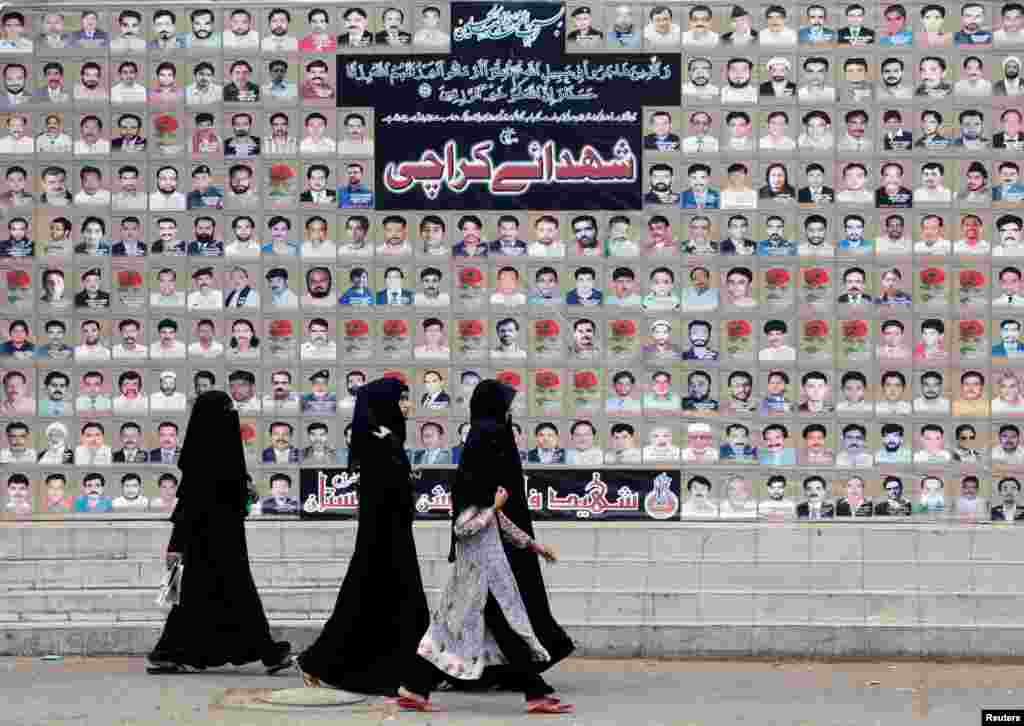 Shi'ite Muslim women walk past a wall with portraits of the victims killed in a bombing in a residential area in March 2013, during the Shi'ite Youm Ali procession in Karachi, Pakistan.