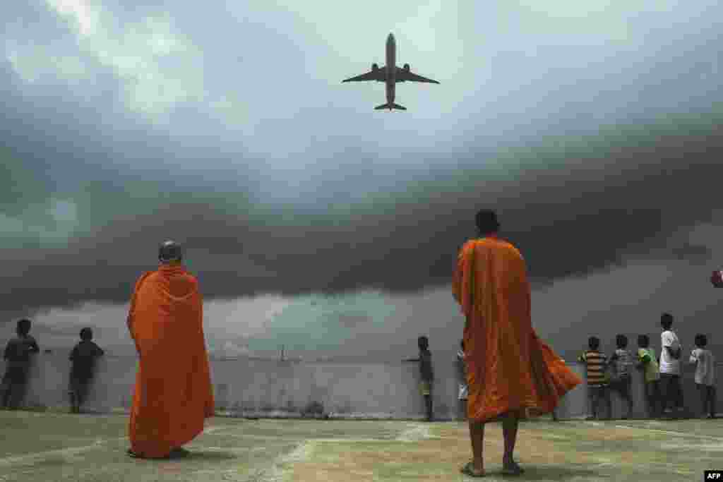 Buddhists monks and children look at an international passenger flight taking off at the Netaji Subhash Chandra Bose International Airport, from the rooftop at a Buddhist mission hostel and school for underprivileged children in in Kolkata, India.