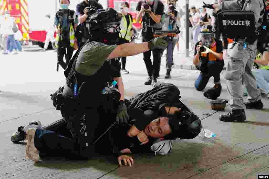 A police officer raises his pepper spray handgun as he detains a man during a march against the national security law at the anniversary of Hong Kong's handover to China from Britain.