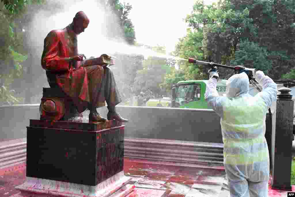 A municipal employee cleans a statue of a famous Italian journalist Indro Montanelli in a Milan public square, a day after it was defaced, stained with red paint and tagged with the inscription "racist, rapist."