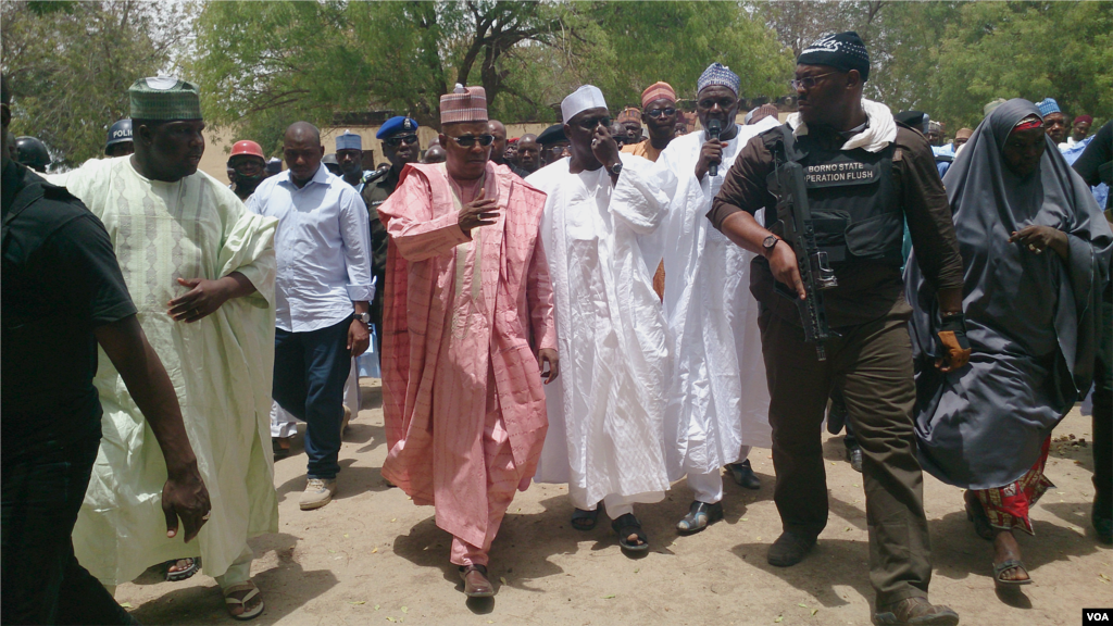Uma comitiva composta pelo Governador de Chibok, o comissário local para a educação (segurando o microfone), segurança armada e pessoas da cidade caminham em direcção ao local da escola secundária queimada, Chibok, Nigéria, Abril 21, 2014. (Anne Look/VOA)