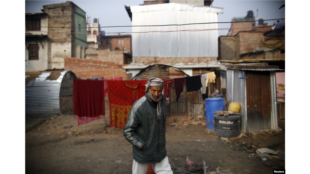 FILE - A man walks past a temporary shelter built near houses which were damaged during the earthquakes last year, in Bhaktapur, Nepal.