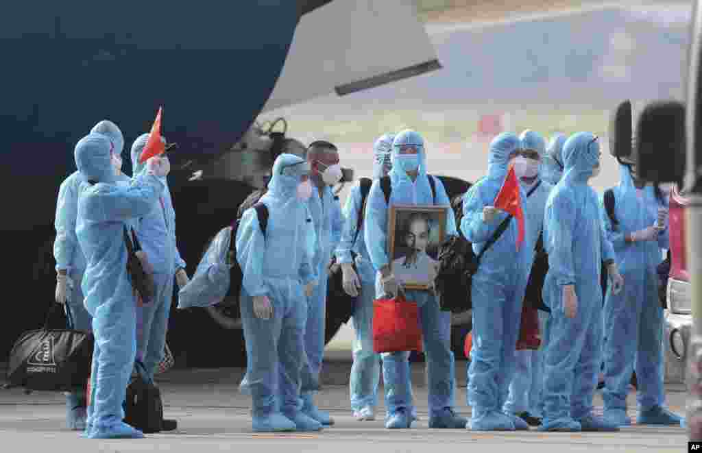 Vietnamese COVID-19 patients in protective gear, holding Vietnamese flags and carrying a portrait of the national leader Ho Chi Minh, arrive at the Noi Bai airport in Hanoi. One hundred and twenty nine patients who were working in Equatorial Guinea are brought home in a repatriation flight.