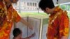 FILE - Dancers from the hula group Na Lei Hulu I Ka Wekiu look at a display of Hawaiian language newspapers on the Iolani Palace grounds in Honolulu, July 21, 2012.