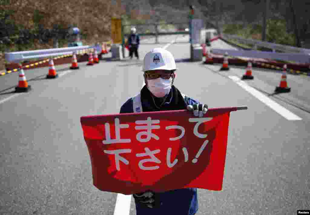 Petugas keamanan memegang bendera bertuliskan "Berhenti!" di gerbang yang menandai perbatasan antara kota Tamura dan Okuma di Okuma, prefektur Fukushima (1/4).
