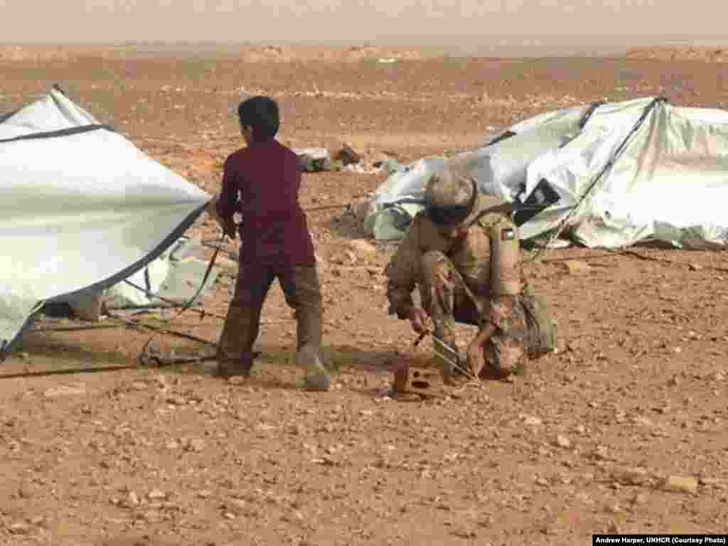 A Jordanian soldier helping a young Syrian refugee put back up a tent blown down by the relentless wind. The UNHCR calls Jordan the "model host."