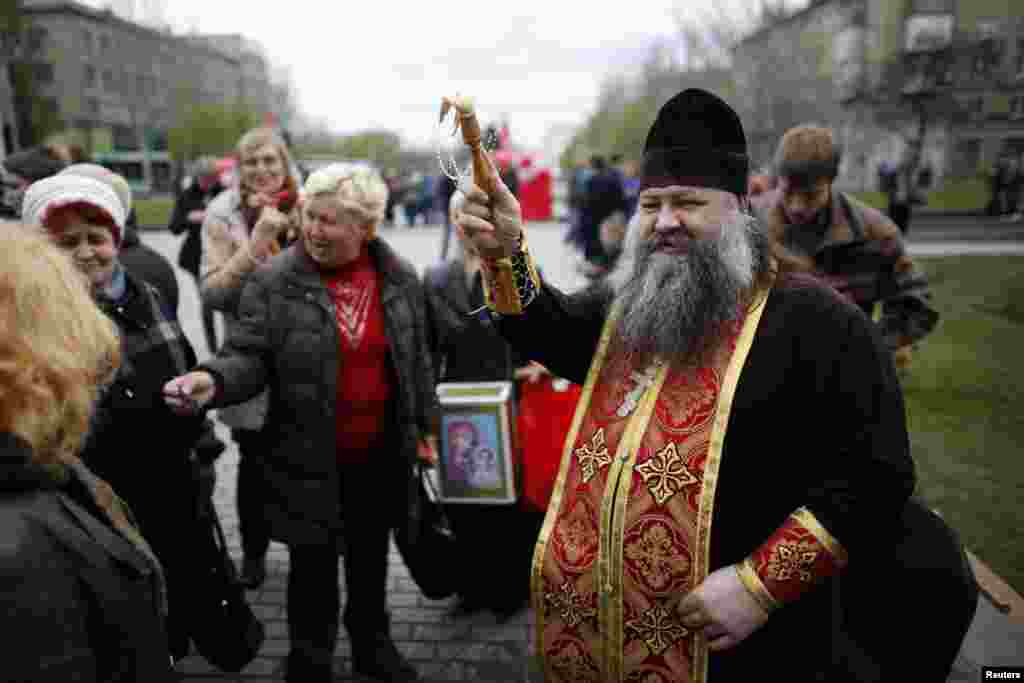 Seorang pendeta Ukraina memercikkan air suci pada jemaat di luar gedung pemerintah daerah pada perayaan Paskah di Donetsk, Ukraina timur. (Reuters/Baz Ratner)