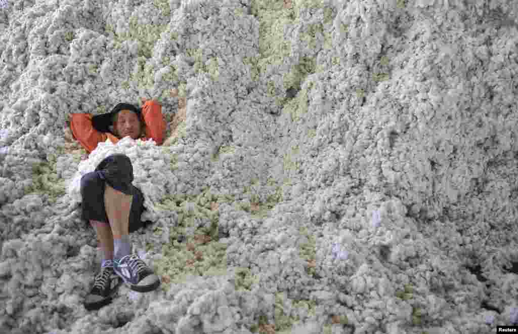 A worker rests on piles of cotton at a ginning factory in Wuhu, Anhui province, China