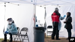 Un trabajador, a la izquierda, descansa por un segundo entre los pacientes, mientras otra persona, a la derecha, se hace el test de COVID-19 en un centro de pruebas ambulante en Farragut Square, el 23 de diciembre de 2021, a pocas cuadras de la Casa Blanca en Washington.